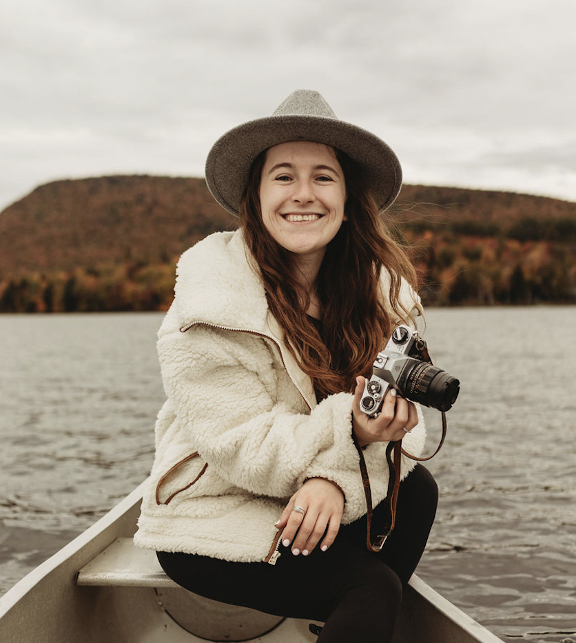 Adventure photographer holding a camera on a canoe in the autumn in New York adirondak's on a weekend getaway at an airbnb